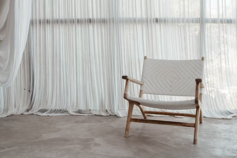 Wooden chair with white woven seat in front of sheer curtains.